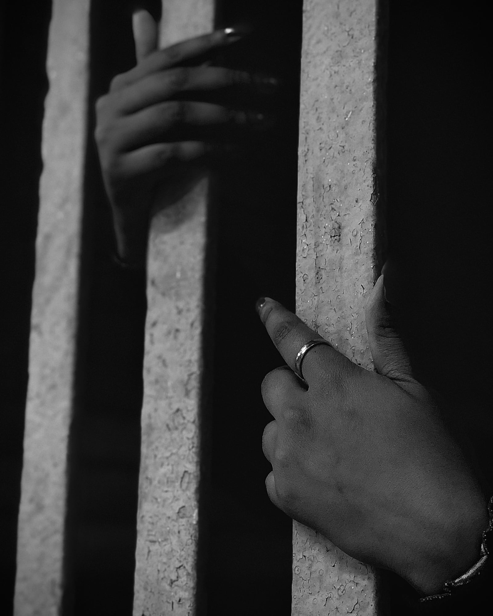 Two hands gripping the bars of a cell door, photographed in black and white