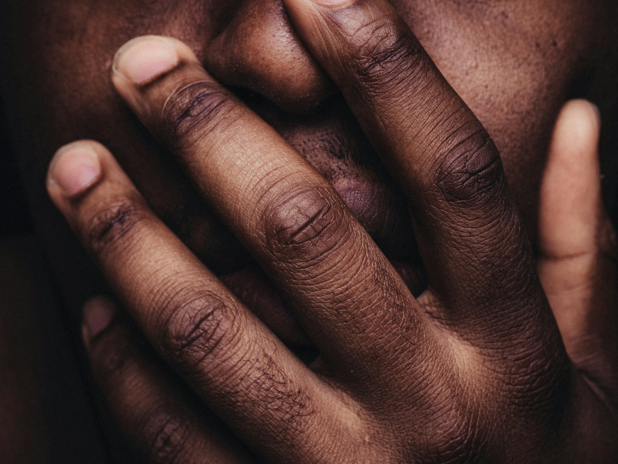 Hands clasped over a person's face in low light